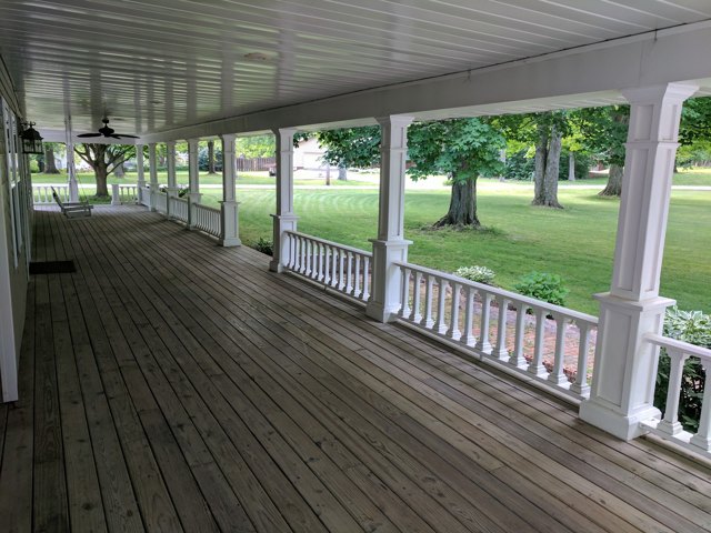 A sheltered porch with white columns, railings, and a view across the lawn.