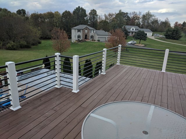 Horizontal railings and white posts follow a deck and staircase beside a landscaped slope.