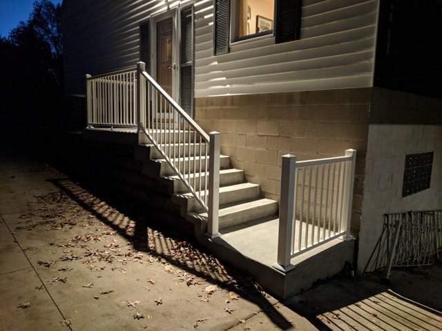 An evening view of a stairway with white railings and illuminated treads.