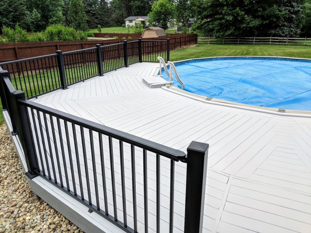 A pale deck platform with dark railings at the edge of an above-ground pool.