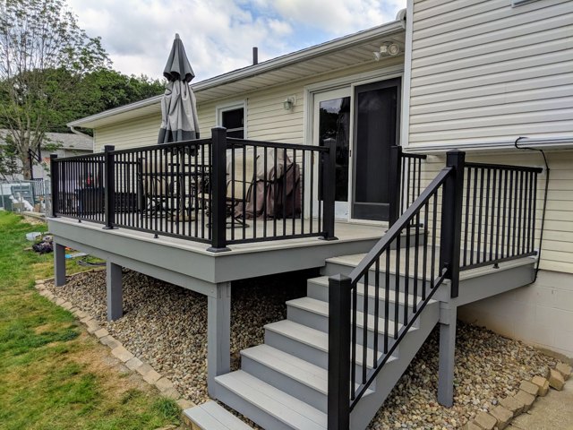 A raised deck with dark railings and stairs leading to the lawn.