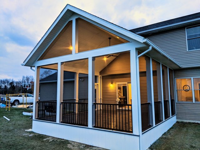 A gabled screened room with warm ceiling lighting and an adjoining deck.