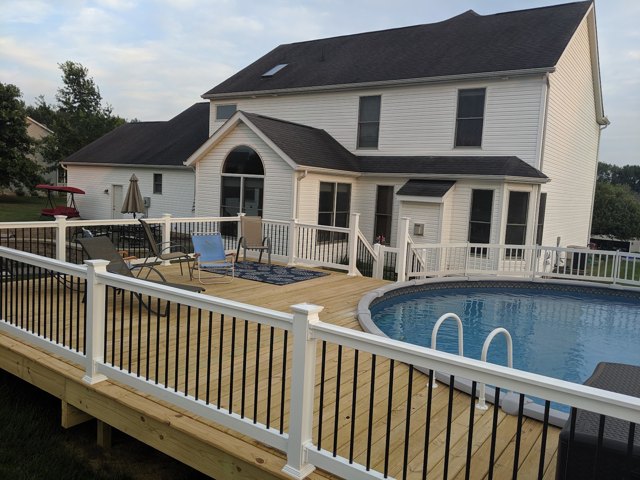 A natural wood pool deck with white posts and contrasting balusters.