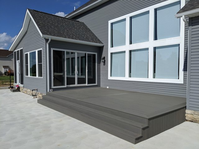 A broad gray deck and generous steps beside the house and swimming pool.