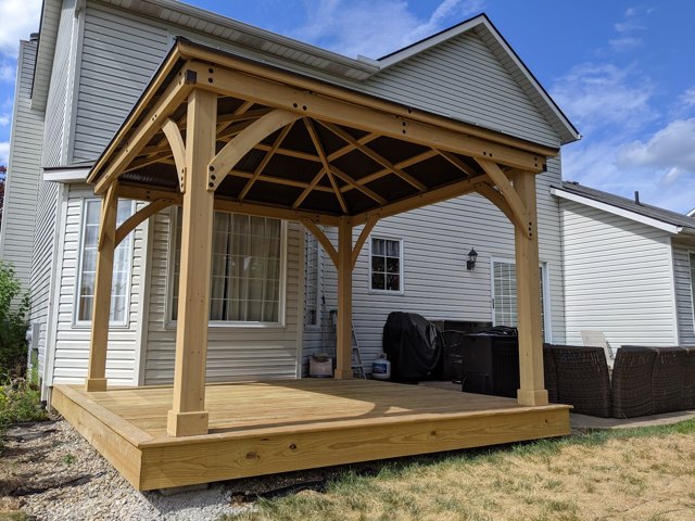 An open timber roof shelters a wood deck beside the house.