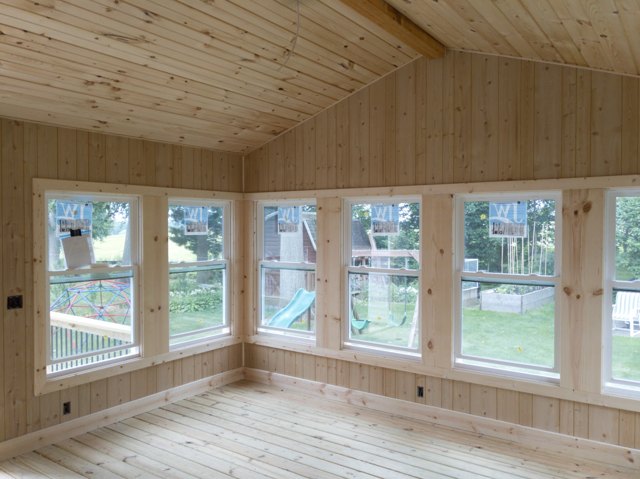 A wood-lined sunroom with broad windows and a deck outside.