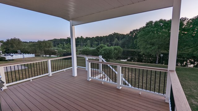 A sheltered deck with white posts, dark balusters, and an open backyard view.
