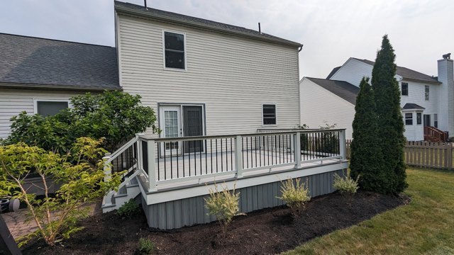 A deck with pale railings follows the home beside a landscaped garden.
