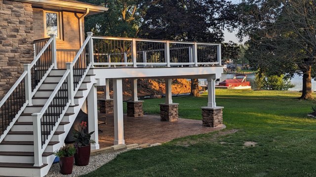 An elevated deck with stone-faced column bases, a pergola, and a patio underneath.