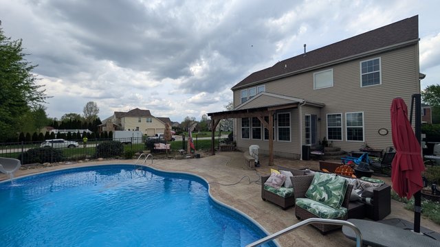 A wide view of the pool, patio, and outdoor seating beside the home.