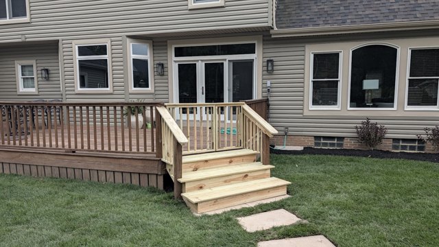 A low wood deck with railings and broad steps down to the lawn.