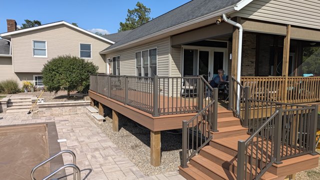 A warm-toned deck with dark balusters and a wide set of steps beside the patio.