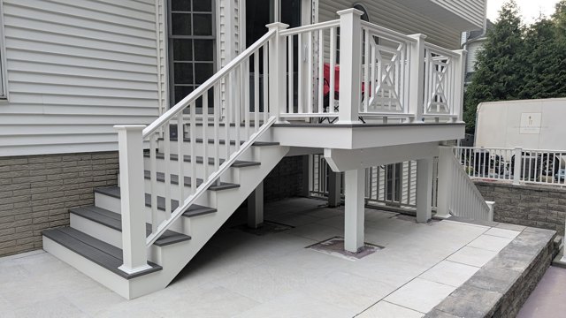 A gray deck with white railings and stairs above a paved patio.