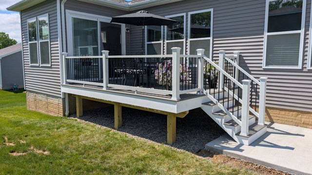 Gray decking, white posts, and dark balusters connect a dining area with the patio and lawn.
