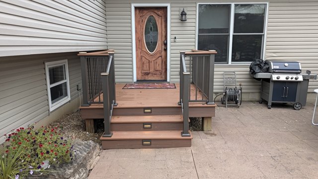 A warm-toned entrance deck with black railings and matching steps.